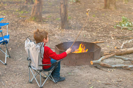 Boy burning a stick in the camp fire while sitting in the chair during winter school holidays, Kuitpo forest, South Australiaの写真素材