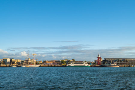 Port Adelaide, Australia - November 9, 2019: Iconic Port Adelaide shore with historic lighthouse and Dolphin Explorer boat viewed across the Port River from the opposite bank at sunset timeのeditorial素材