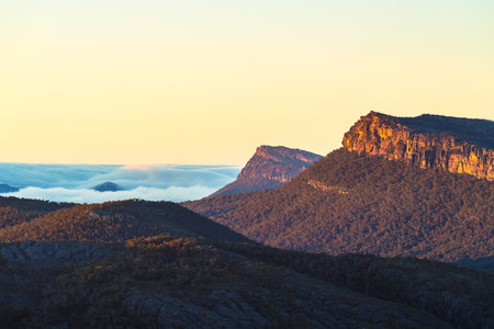 Grampians mountains cliffs at sunrise with clouds below its peaks while viewed from Boroka Lookout, Victoria, Australiaの写真素材