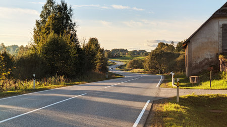 Peaceful Country Road Curving Through Green Countryside at Golden Hour Sunsetの写真素材