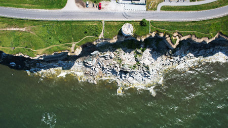 Aerial Top View of Coastal Cliffs, Crashing Waves, and Winding Seaside Road in Estoniaの写真素材