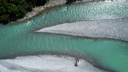A drone view of the turquoise alpine Lech River flowing around bright gravel bars and forested banks...