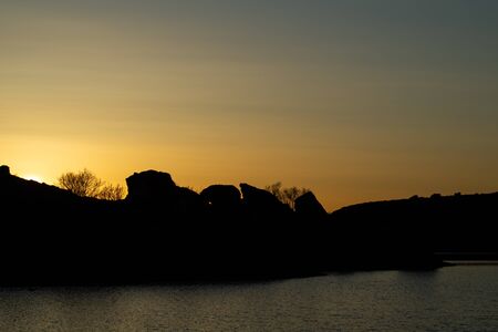 Sunset from a mountain lake with tree and dark mountain sideの写真素材