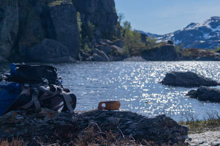 Backpack with wodden cup besides a lake and snowy mountains in bakcgroundの写真素材