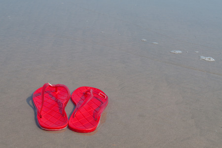 Red slippers on the sand and sea.の写真素材