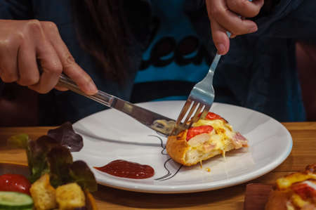 Female hands holding fork and knife to cut a slice of pizza on white plate, selective focusの写真素材