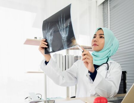 The doctor, a beautiful young Islamic woman had a stethoscope sitting analyzed and pointed and look at the x-ray film. She was confident that the scan results were successful in the examination room.の写真素材