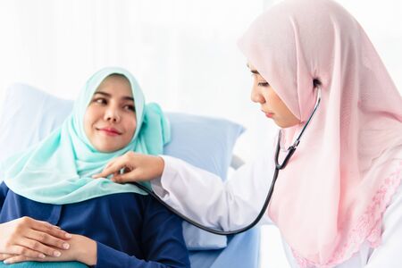 A young beautiful Muslim doctor is using a stethoscope to listen to the patient's heartbeat at the bed in the hospital examination room. Selective focusの写真素材