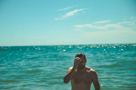 Handsome man coming out of turqouise sea during sunny day on the beachの写真素材