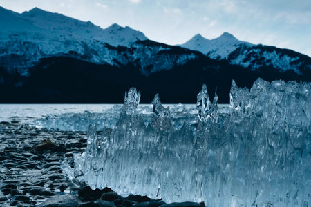 Ice Formation on Alaska Beach with Large Mountains Covered in Snow with Sunny Skies on Cold Dayの写真素材