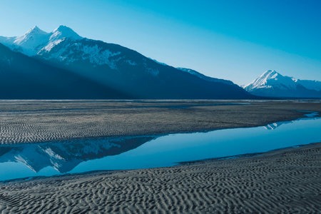 Light Beams Cross Mountain Peaks to River at Valley Floor on Sunny Day with Bright Blue Sky in Alaskaの写真素材