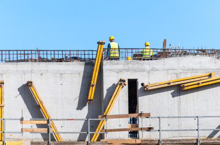 Construction workers collaborating on concrete building structure under clear sky