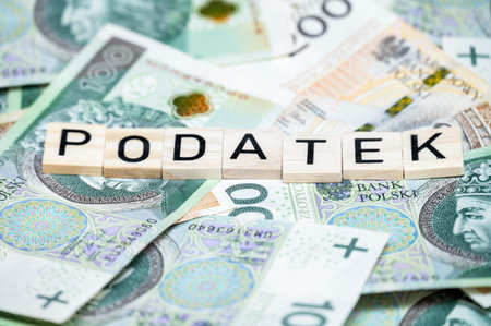 Wooden letter blocks spell 'PODATEK' (tax in Polish) on a background of scattered Polish zloty...