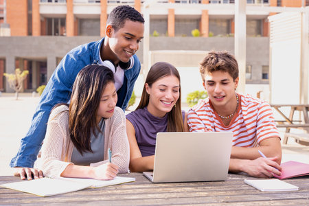 A group of students with laptops sit near the campus and communicate.