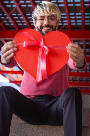 Vertical portrait young smiling man holds a heart-shaped gift box. Loversの写真素材