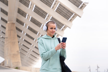 A smiling female runner takes a break to use an app on her smartphone outdoors.