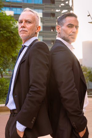 Vertical portrait two successful businessmen standing back to back looking at camera,の写真素材