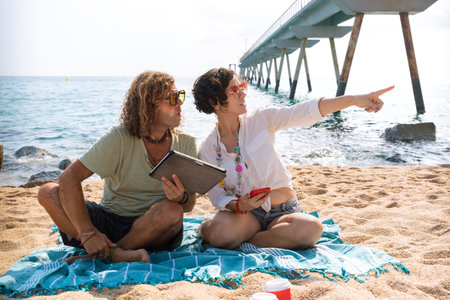 Couple on the beach,pointing to the location of the hotel with the tabletの写真素材