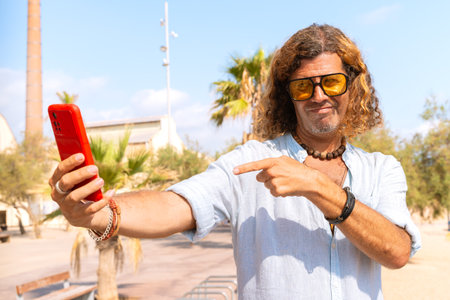 A smiling man with a smartphone taking a selfie looks at the camera and smiles.