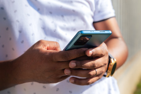 Glamorous smiling black man, sitting using a social media app on a smartphone.の写真素材