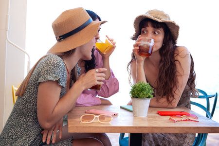 Three young friends in summer dresses having a soft drink in a restaurantの写真素材