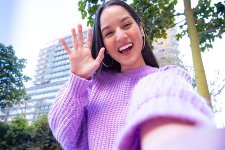 Young latin woman having a video call with cell phone and smiling outdoors.の写真素材