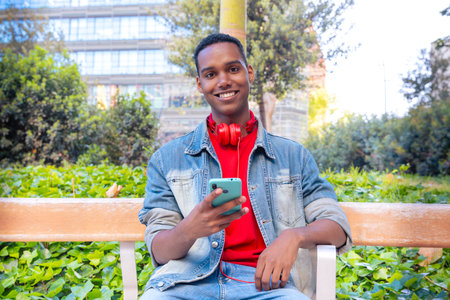 Portrait of a smiling young african american man with a smartphone surfing the internet outdooors.
