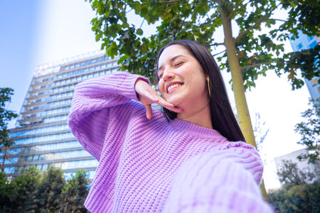 Young woman having a video call with cell phone and smiling outdoors.の写真素材