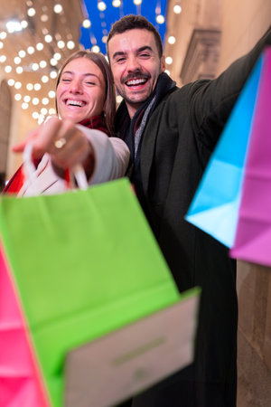 Happy couple showing colorful shopping bags on festive city street at nightの写真素材