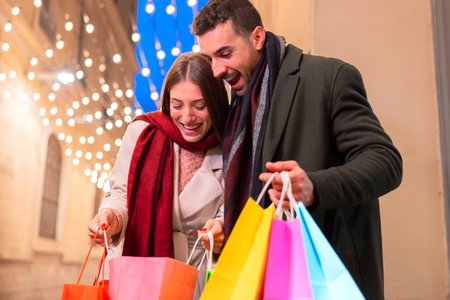 Couple surprised with shopping bags festive city night Christmas joyの写真素材