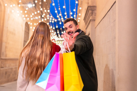 Smiling couple with shopping bags walking on festive city street at nightの写真素材