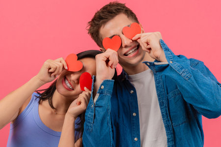 Playful Couple Holding Heart Shapes on Pink Backgroundの写真素材