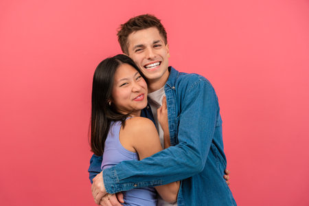 Happy young couple embracing and smiling against a pink backgroundの写真素材