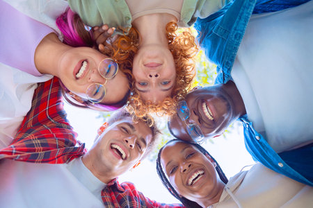 Group of diverse young people smiling and looking down in a circle outdoorsの写真素材