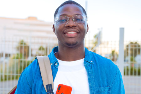 Smiling Student with Glasses Holding Red Smartphone Outdoorsの写真素材