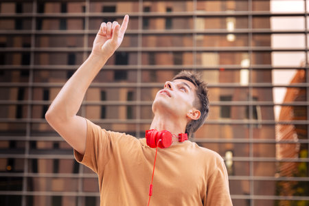 Young Man Pointing Upward with Red Headphones Around His Neckの写真素材
