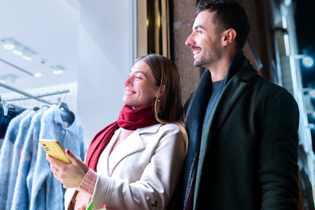 Couple smiling with smartphone shopping festive store display city night holidayの写真素材
