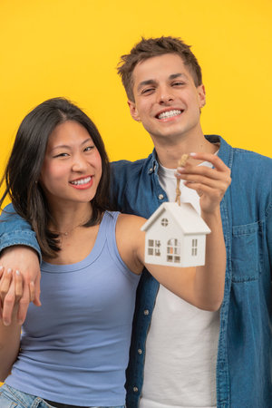 Happy couple holding house keys and small model house, celebrating new homeの写真素材