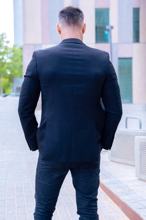Rear view businessman in black suit posing confidently in urban setting.Verticalの写真素材