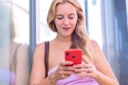 Blonde Woman Using Smartphone Outdoors in Urban Settingの写真素材
