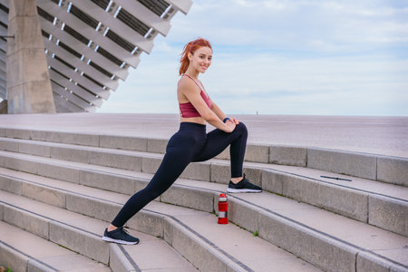 Fit Young Woman Stretching on Outdoor Stairs in Urban Settingの写真素材