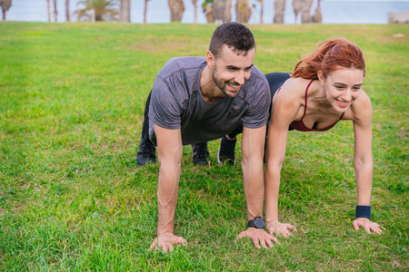 Fit couple exercising outdoors doing push-ups on the grass in a park