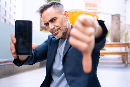 Man Holding Smartphone and Giving Thumbs Down Gesture Outdoorsの写真素材