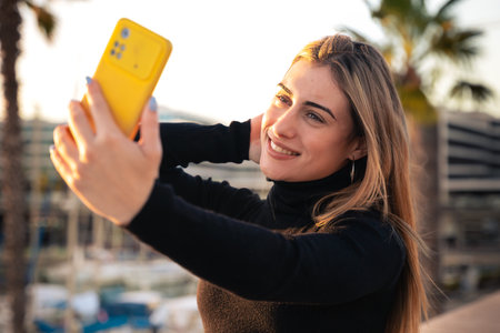 Young caucasian woman having a video call with cell phone and smiling outdoors.の写真素材