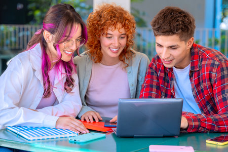 A group of students with laptops sit near the campus and communicate.