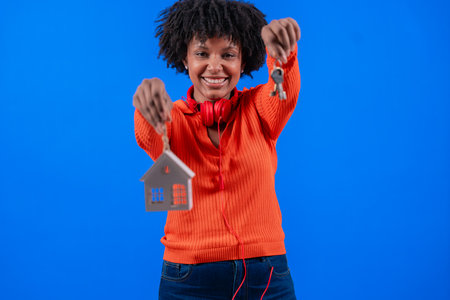 African American woman holding house keys and home model, smiling confidentlyの写真素材