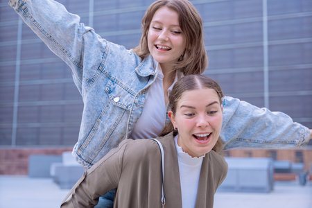 Cheerful Caucasian friends having fun with piggyback ride outdoors in the cityの写真素材