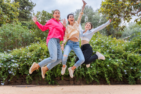 Three joyful young women jumping in the air, celebrating and having fun outdoors.
