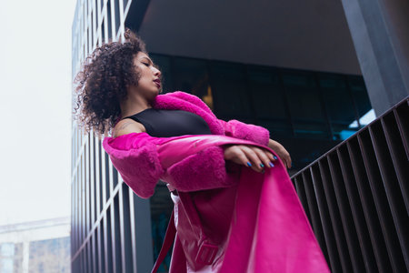 Elegant woman in a pink coat performing artistic movements in an urban settingの写真素材