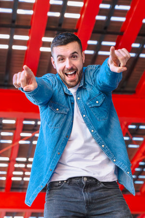 Happy man pointing at camera with both hands, vertical image, red urban backgroundの写真素材